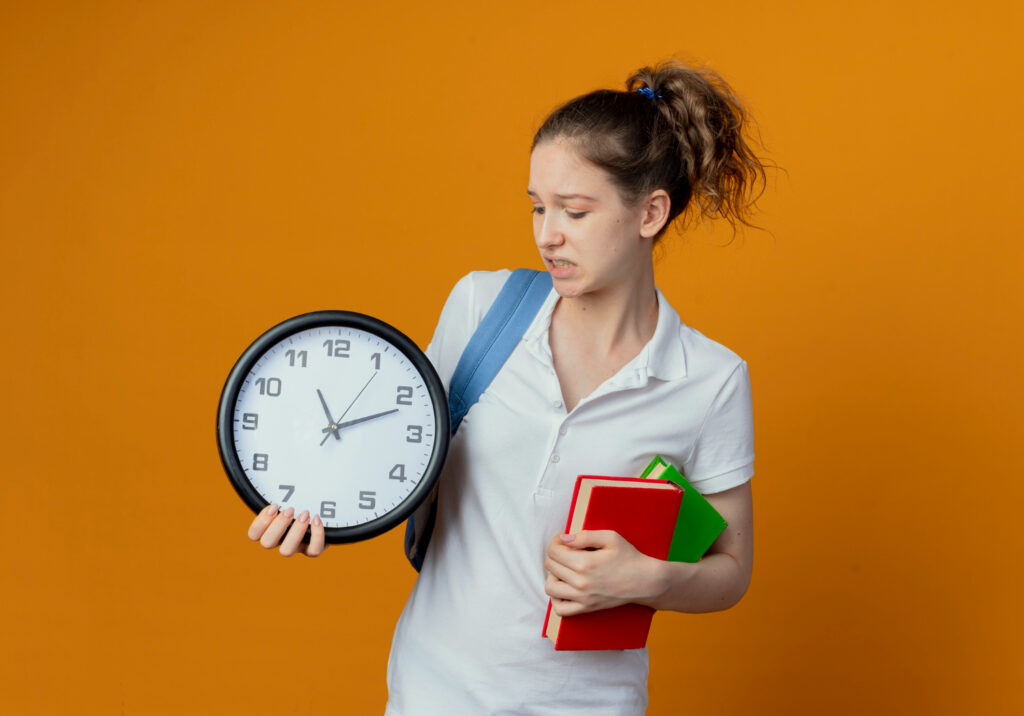 unpleased-young-pretty-female-student-wearing-back-bag-holding-looking-clock-holding-books-isolated-background-with-copy-space
