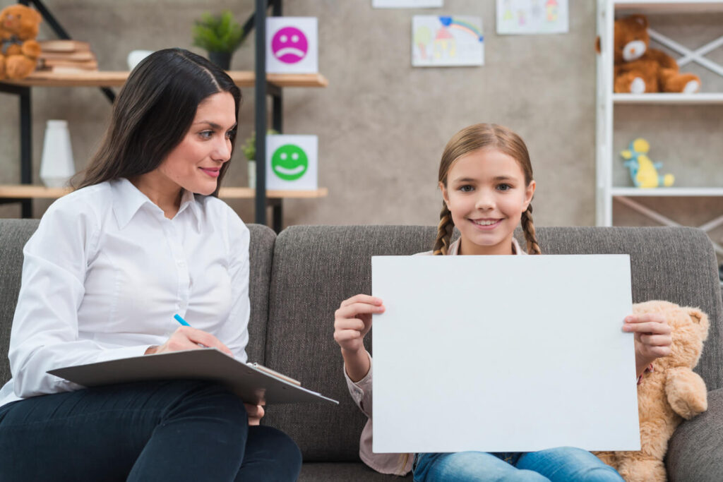 young-female-psychologist-looking-little-girl-showing-blank-white-paper-camera (1)