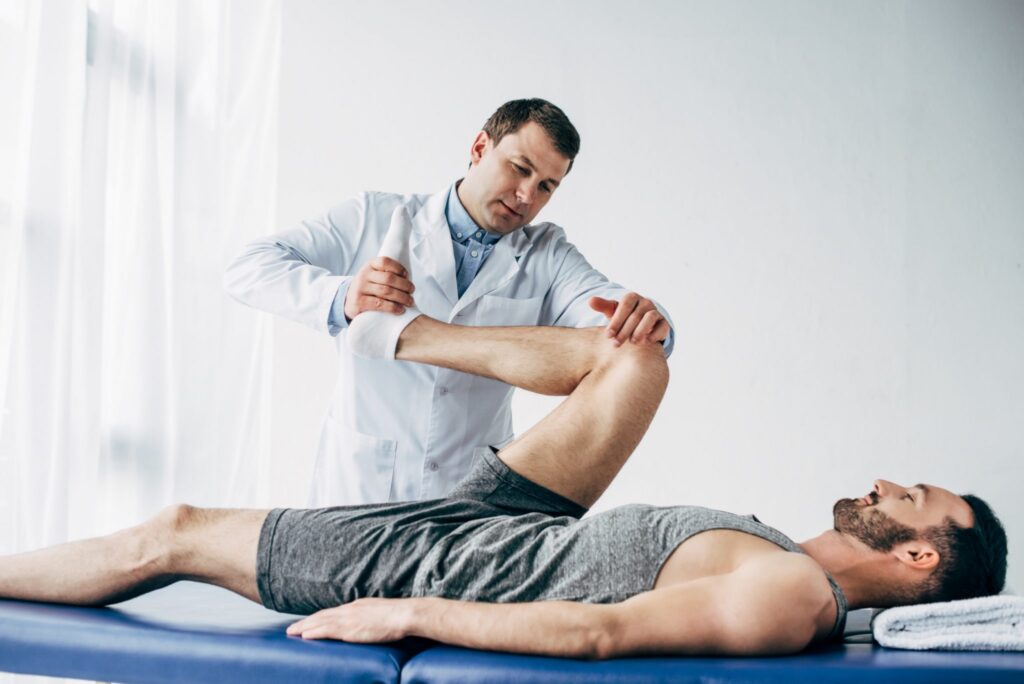 handsome-chiropractor-stretching-leg-of-patient-in-k5sbend-scaled